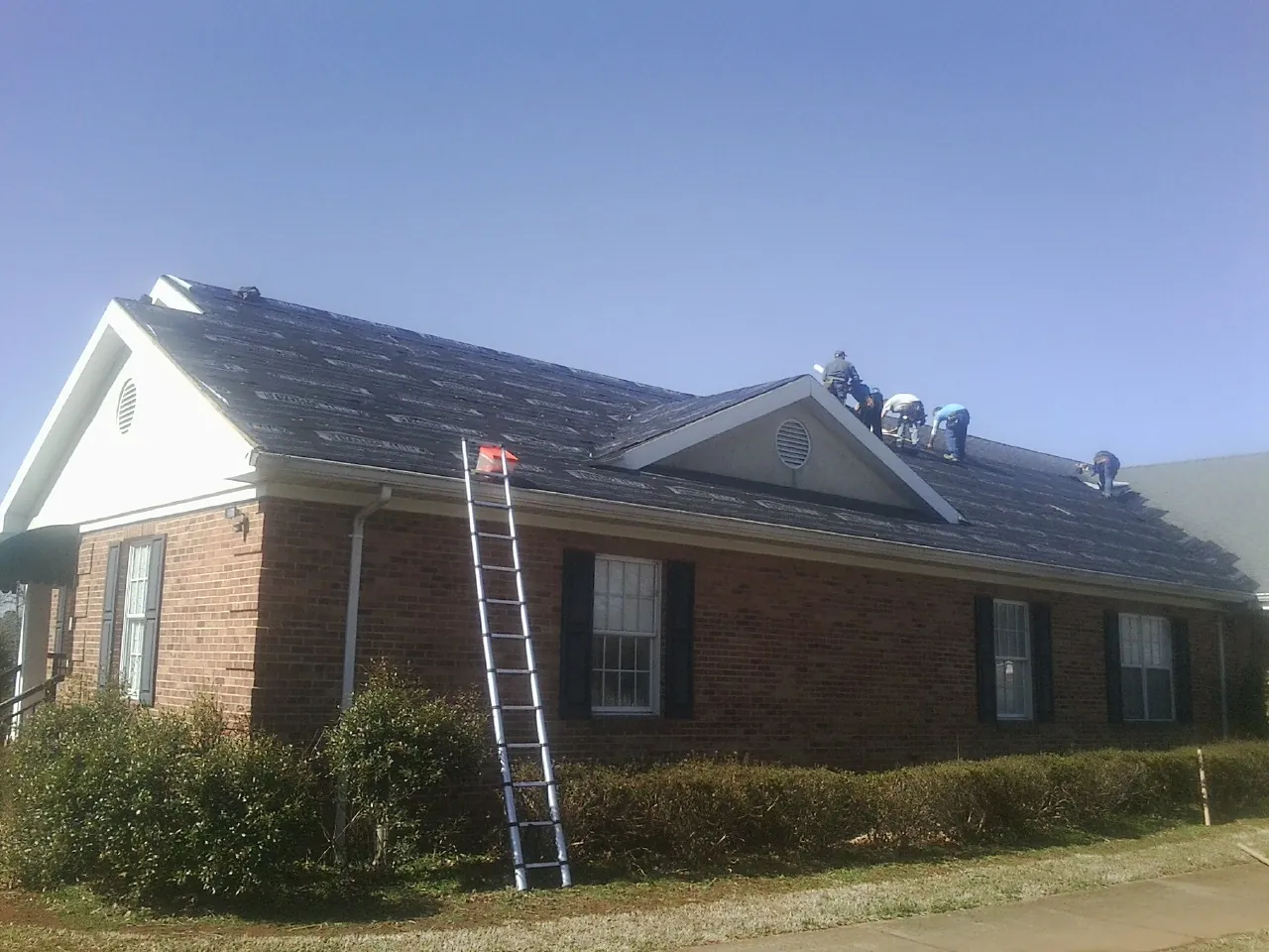 Crew tearing shingles off a brick ranch roof with a ladder set — Emergency Roof Repair work by our crew in Pittsburg