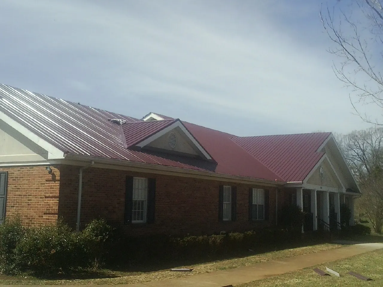 Red metal roof with gabled entries on a long brick building, from a Hail Damage Roof Repair job in Pittsburg
