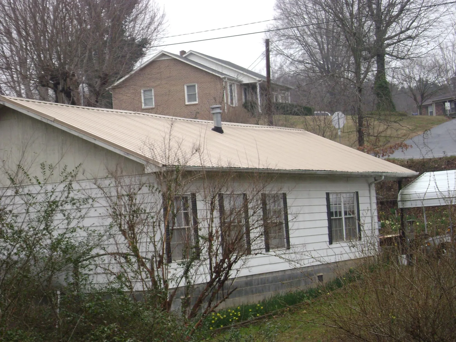 Tan metal roof on a white sided house set into a hillside — Commercial Roofing by Roofing Brothers in Pittsburg