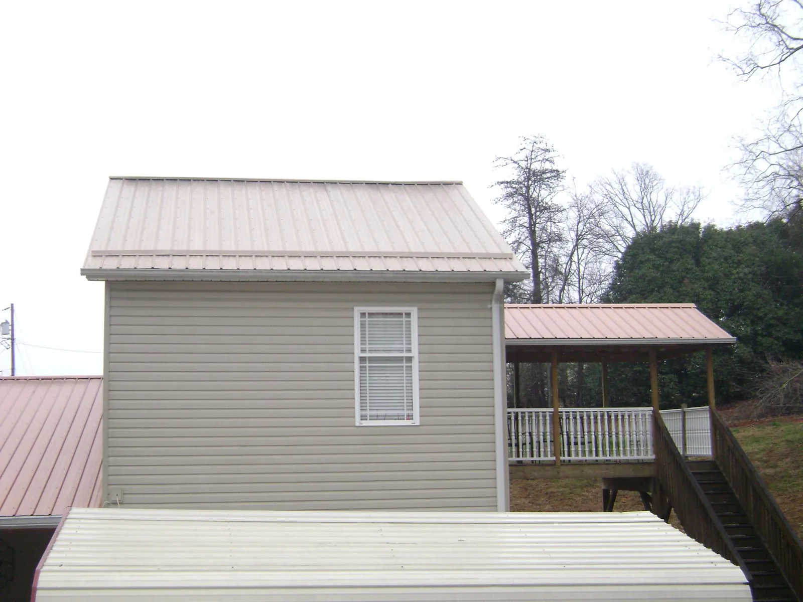 Tan metal roofs on a two story addition and attached porch, from a Roof Replacement job in Pittsburg